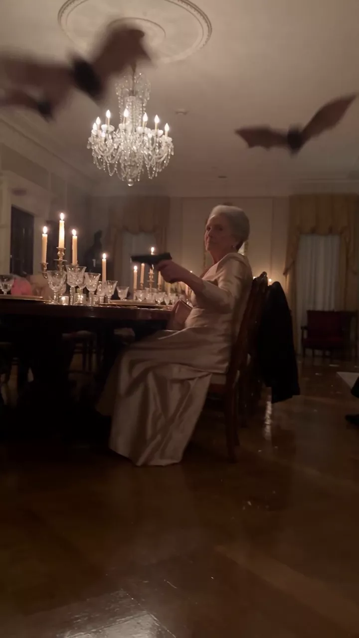 A draft: a formal candlelit dinner under a chandelier; bats show as dark smears across the ceiling and a grandmother in an evening dress fires a handgun upward from her chair