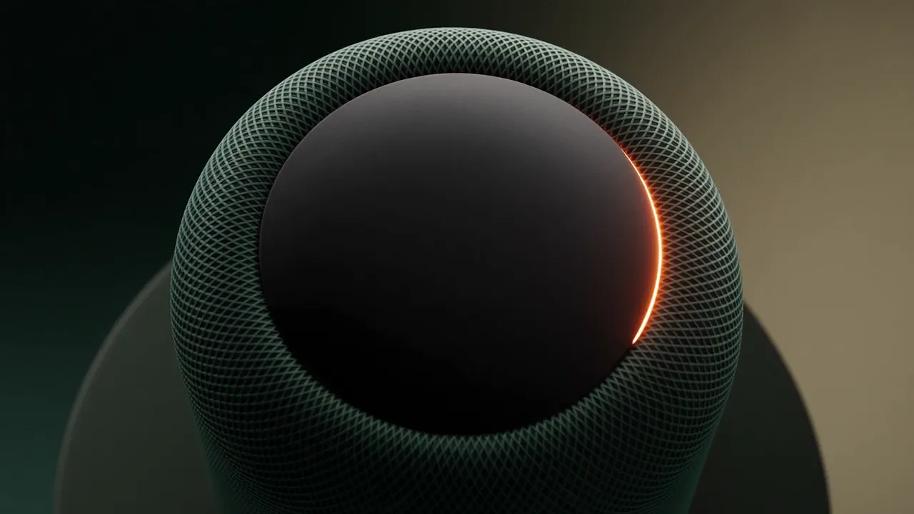 A dark green fabric smart speaker with a brass ring at its base on a black plinth, lit by one amber rim light against a deep green gradient