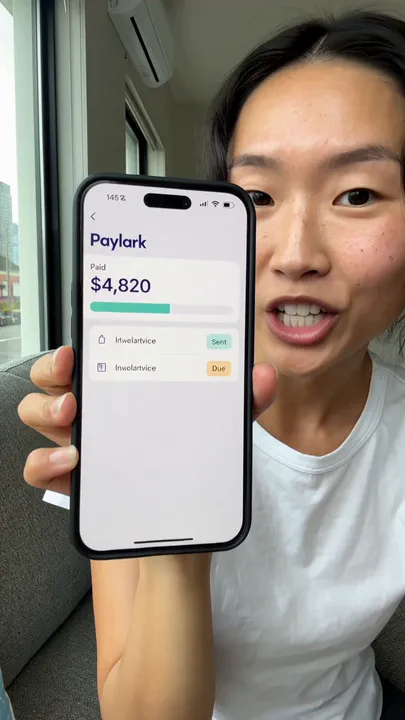 A creator holds a phone close to the lens showing an invoicing app screen with a paid total and two invoice rows.